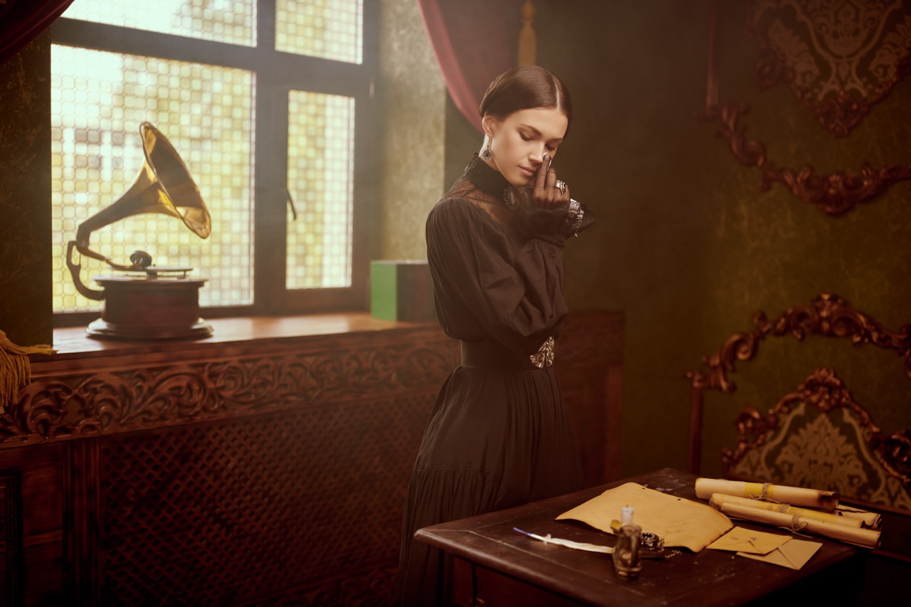 The heroine of the 19th century novel, a dramatic story. A beautiful sad girl of noble origin in a mourning black dress wipes her tears standing in front of a table with a letter on it.
