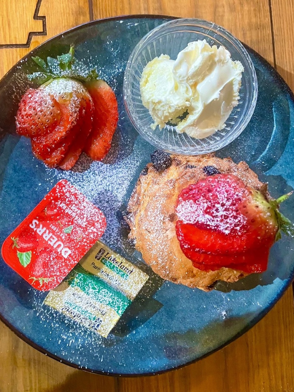A blue plate with a scone, strawberries and cream on it.